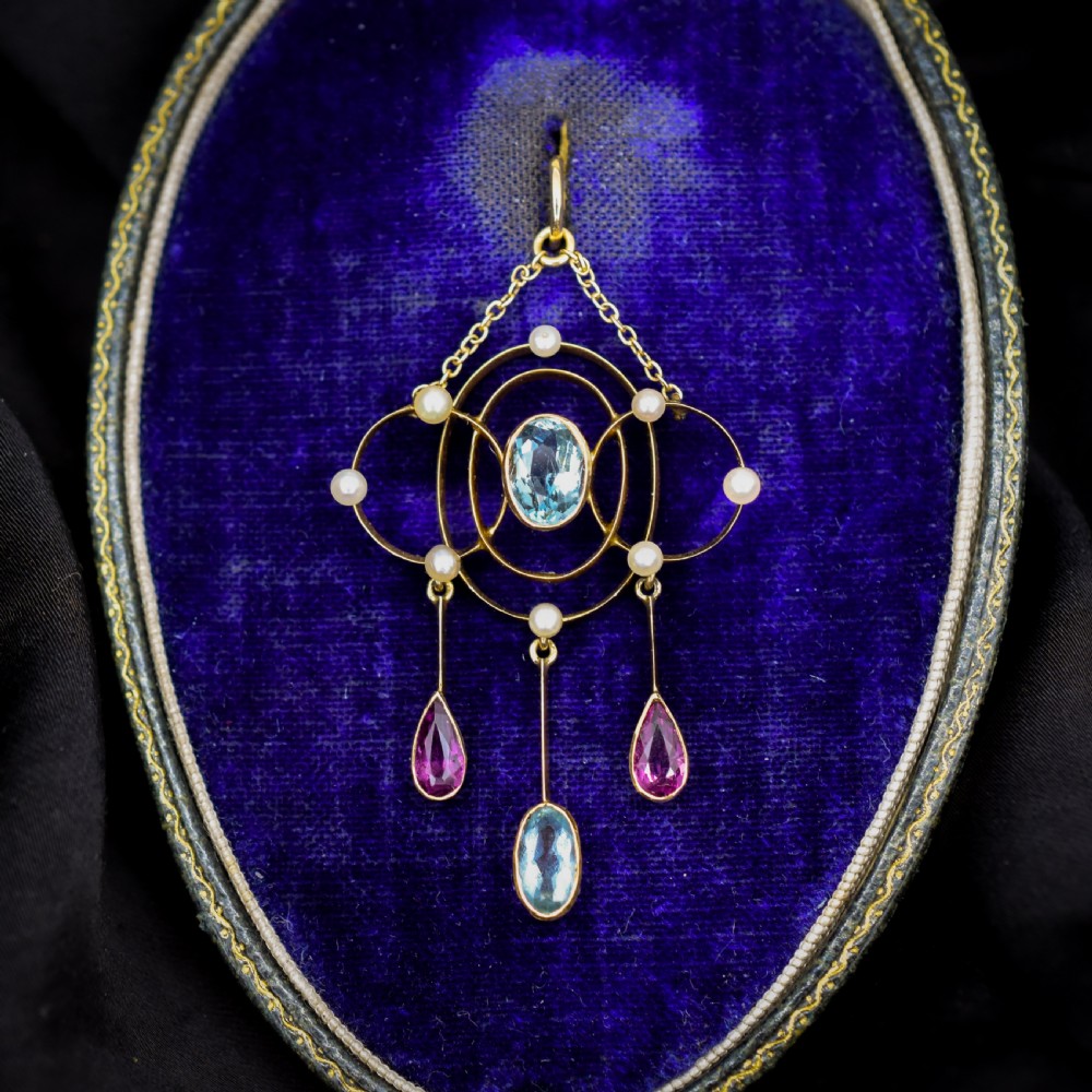 An antique 15ct yellow gold Edwardian lavalier pendant featuring openwork wire design, a central oval aquamarine, seed pearl accents, and three suspended gemstone drops.