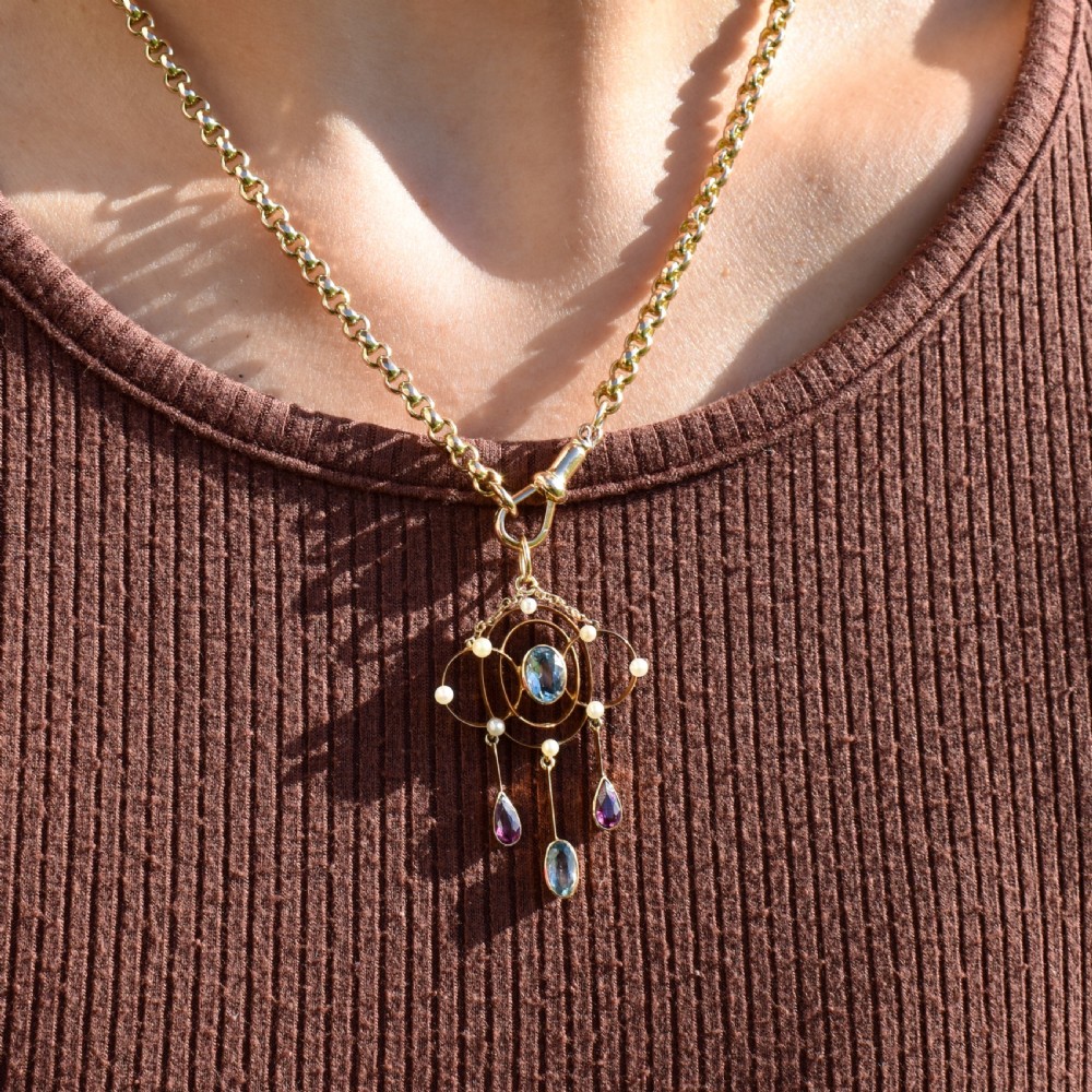 An antique 15ct yellow gold Edwardian lavalier pendant featuring openwork wire design, a central oval aquamarine, seed pearl accents, and three suspended gemstone drops. View II
