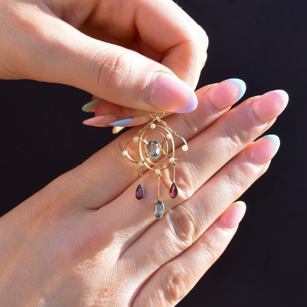 An antique 15ct yellow gold Edwardian lavalier pendant featuring openwork wire design, a central oval aquamarine, seed pearl accents, and three suspended gemstone drops. View III