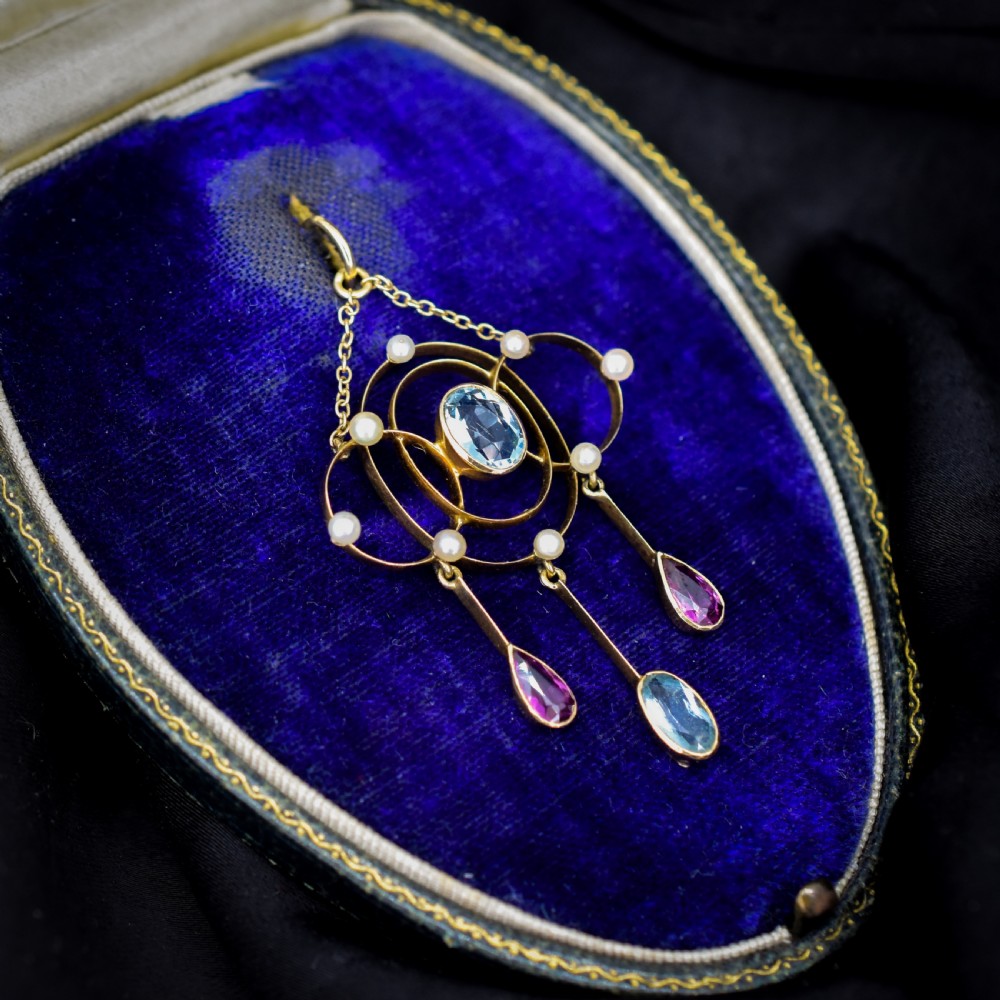 An antique 15ct yellow gold Edwardian lavalier pendant featuring openwork wire design, a central oval aquamarine, seed pearl accents, and three suspended gemstone drops. View IV
