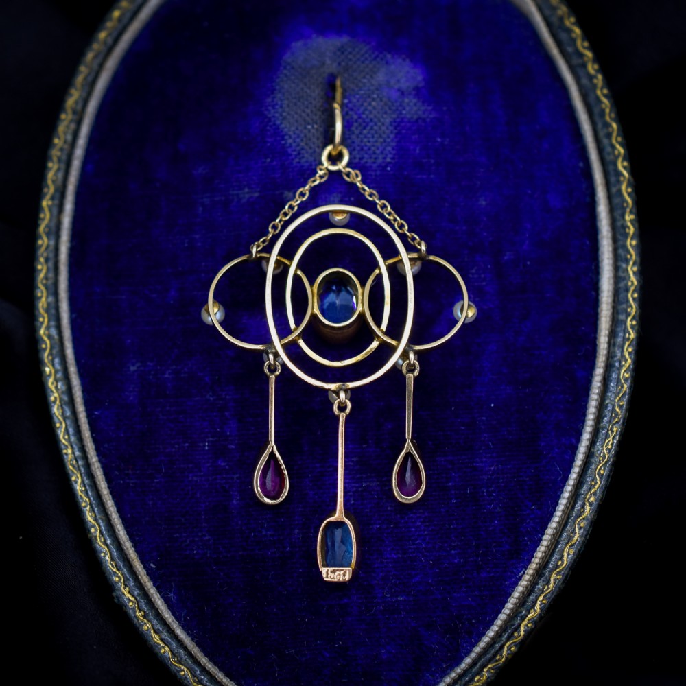 An antique 15ct yellow gold Edwardian lavalier pendant featuring openwork wire design, a central oval aquamarine, seed pearl accents, and three suspended gemstone drops. View V