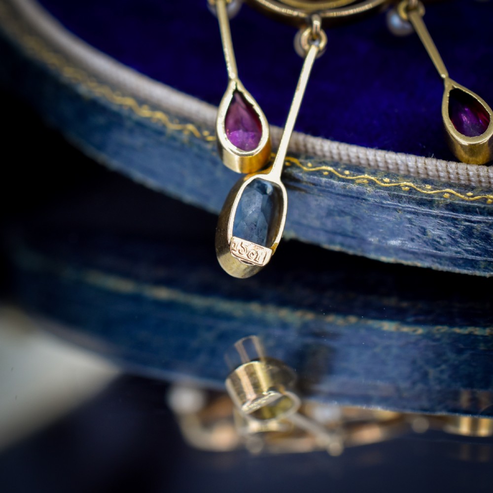 An antique 15ct yellow gold Edwardian lavalier pendant featuring openwork wire design, a central oval aquamarine, seed pearl accents, and three suspended gemstone drops. View VI
