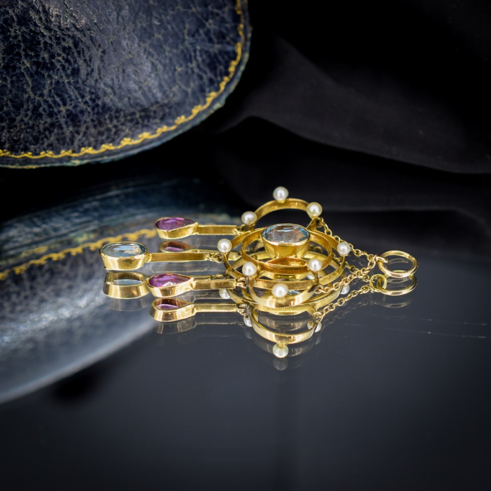 An antique 15ct yellow gold Edwardian lavalier pendant featuring openwork wire design, a central oval aquamarine, seed pearl accents, and three suspended gemstone drops. View VII