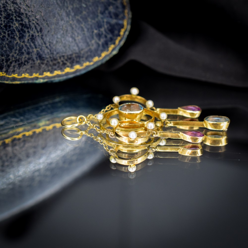 An antique 15ct yellow gold Edwardian lavalier pendant featuring openwork wire design, a central oval aquamarine, seed pearl accents, and three suspended gemstone drops. View VIII