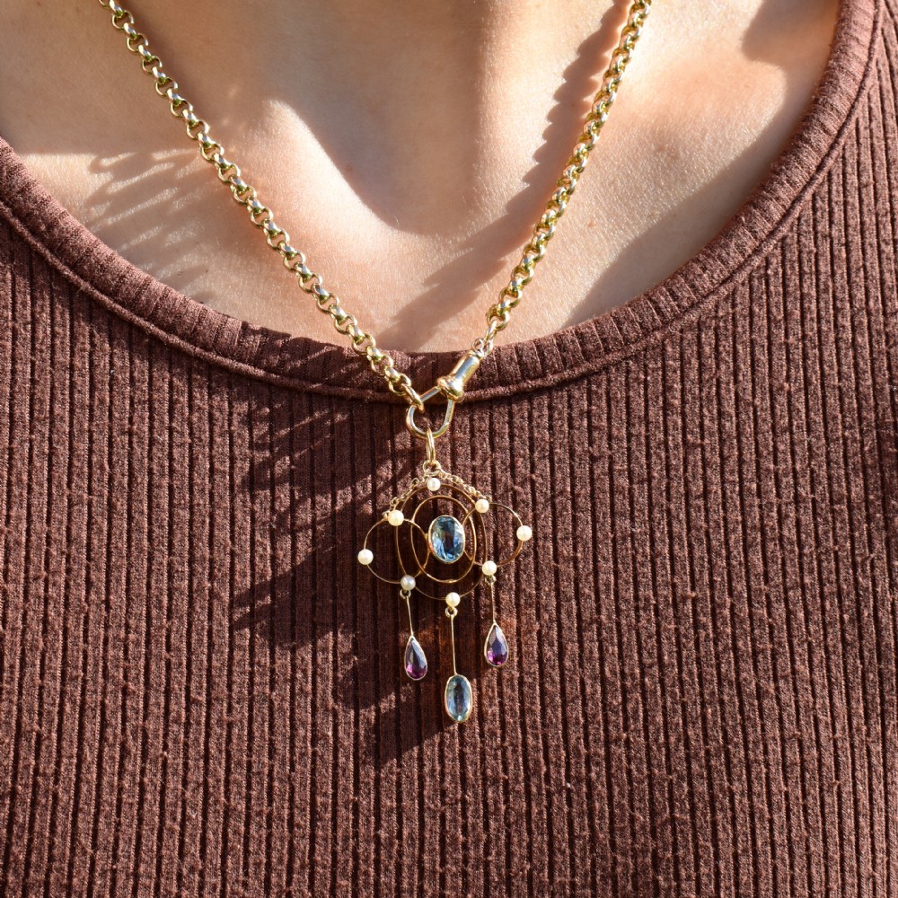 An antique 15ct yellow gold Edwardian lavalier pendant featuring openwork wire design, a central oval aquamarine, seed pearl accents, and three suspended gemstone drops. View IX