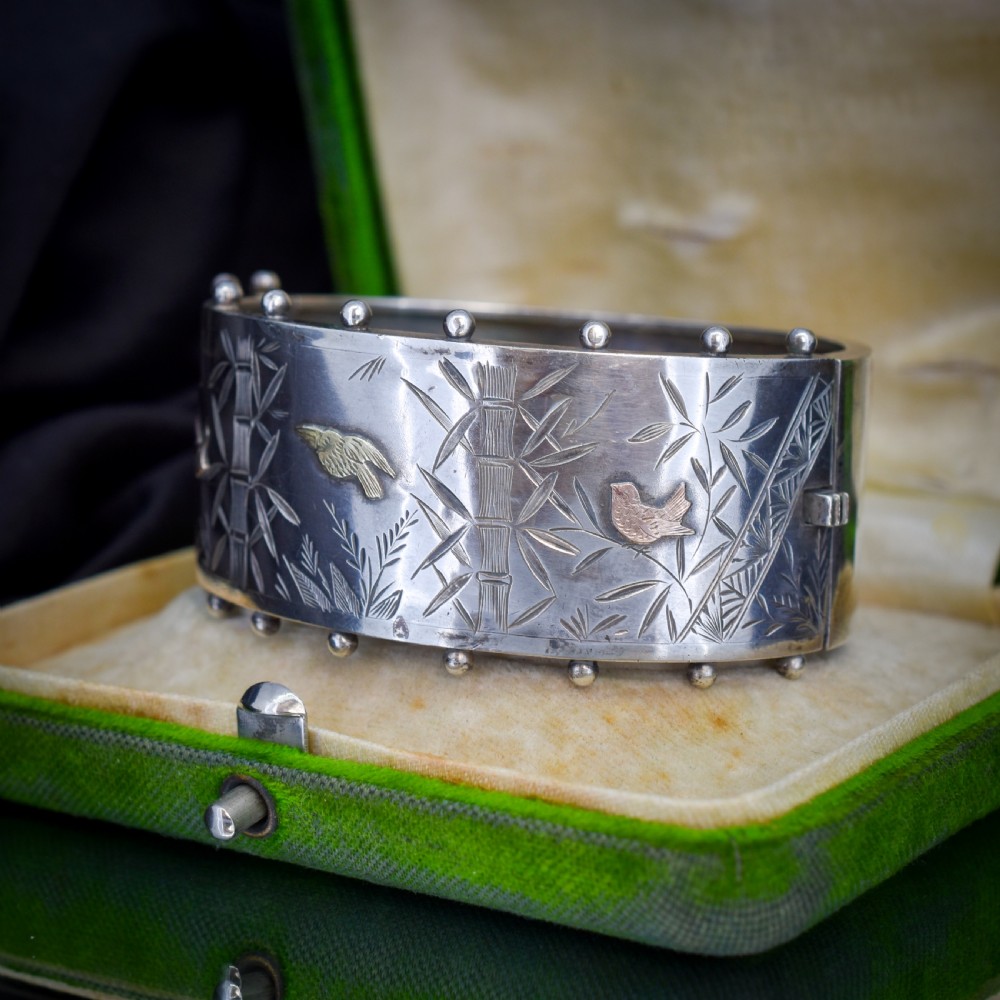 A wide Victorian silver hinged cuff bangle featuring hand-engraved bamboo stalks and foliage, applied gold birds, and beaded studded borders along the top and bottom rims. View II