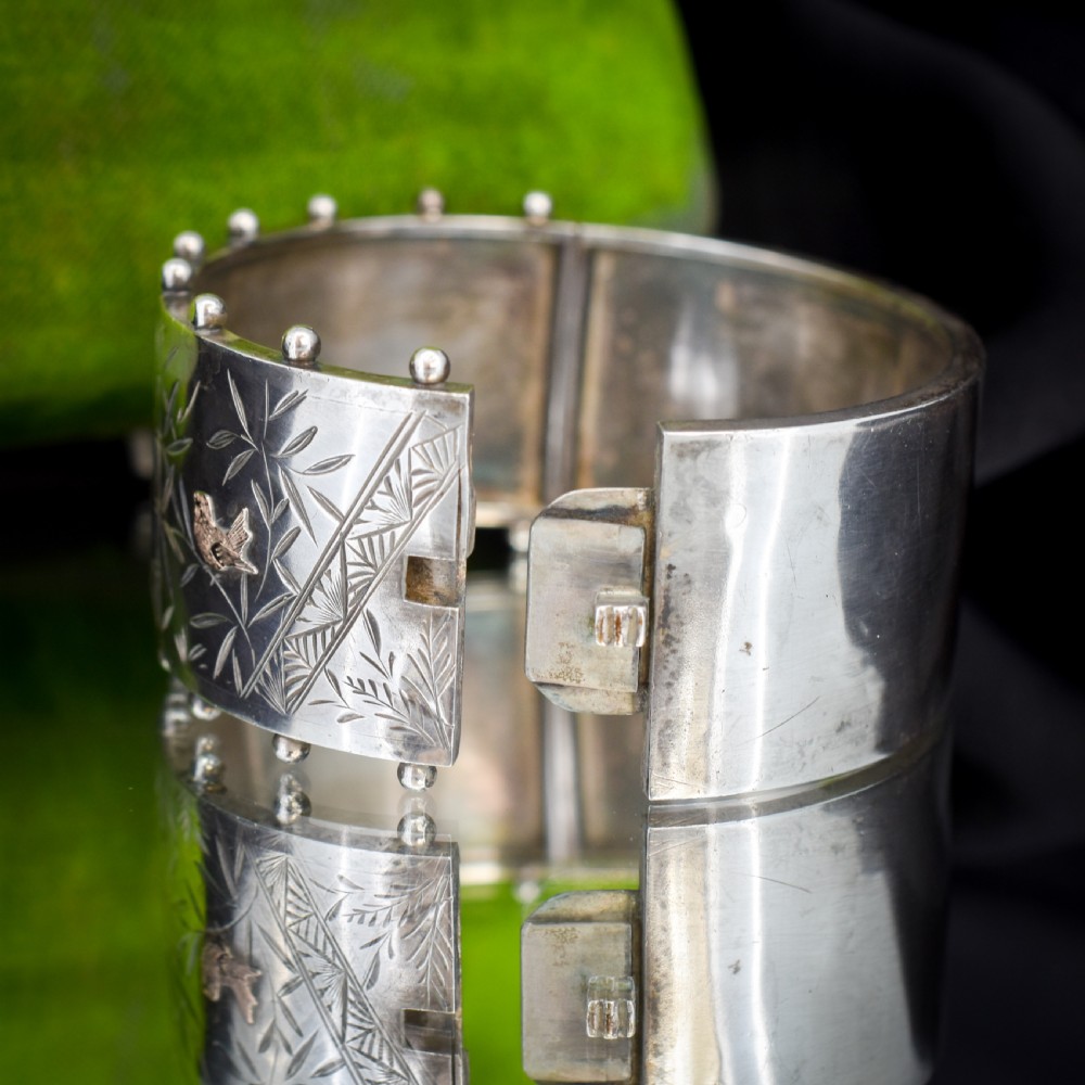 A wide Victorian silver hinged cuff bangle featuring hand-engraved bamboo stalks and foliage, applied gold birds, and beaded studded borders along the top and bottom rims. View IV
