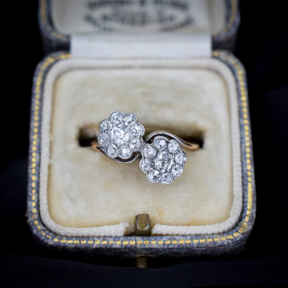 An antique diamond ring featuring two circular daisy clusters on a crossover metal twist band. View II
