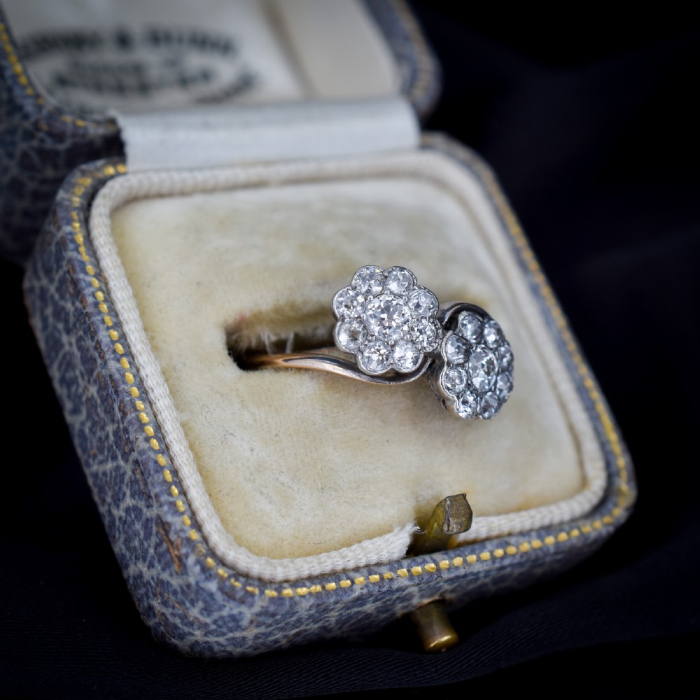 An antique diamond ring featuring two circular daisy clusters on a crossover metal twist band. View III