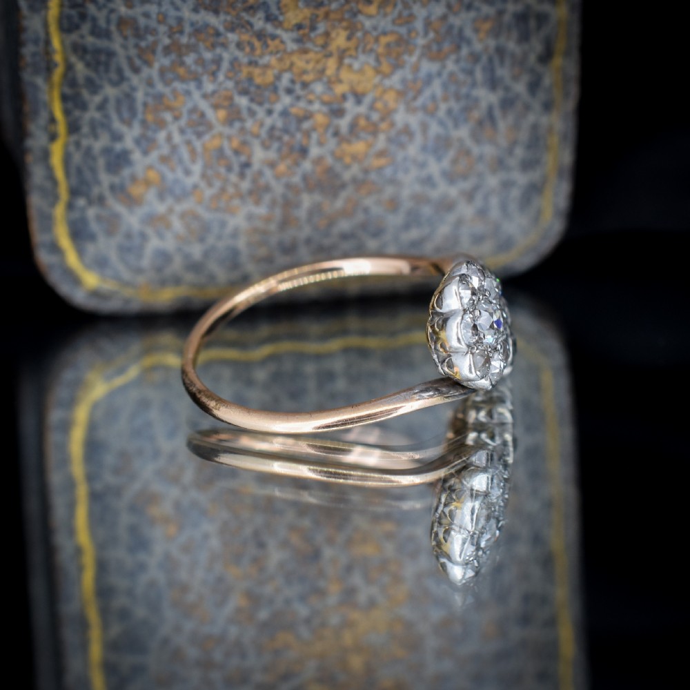 An antique diamond ring featuring two circular daisy clusters on a crossover metal twist band. View V
