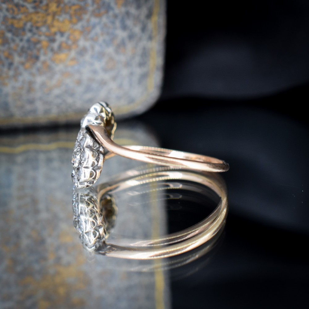 An antique diamond ring featuring two circular daisy clusters on a crossover metal twist band. View VII
