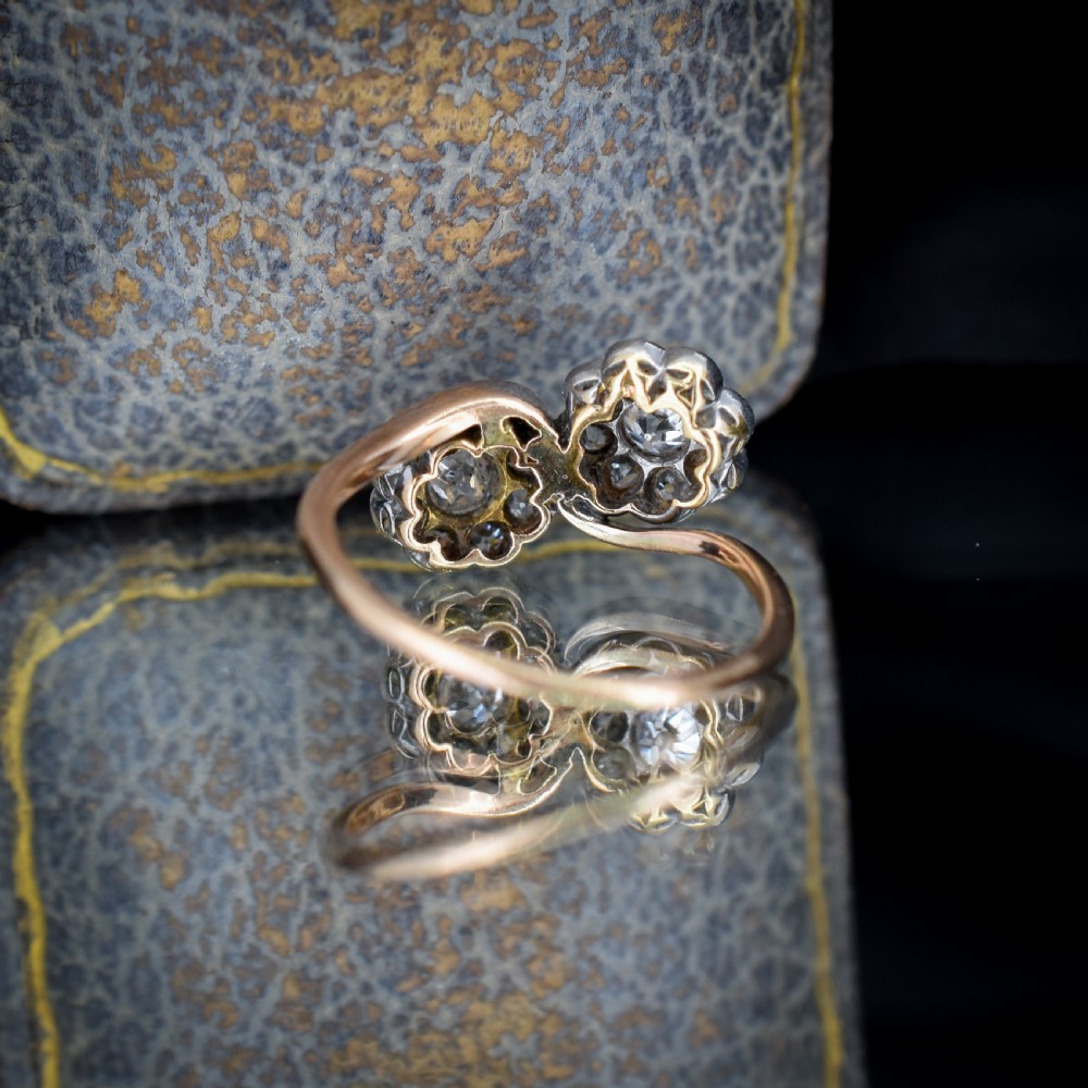 An antique diamond ring featuring two circular daisy clusters on a crossover metal twist band. View VIII