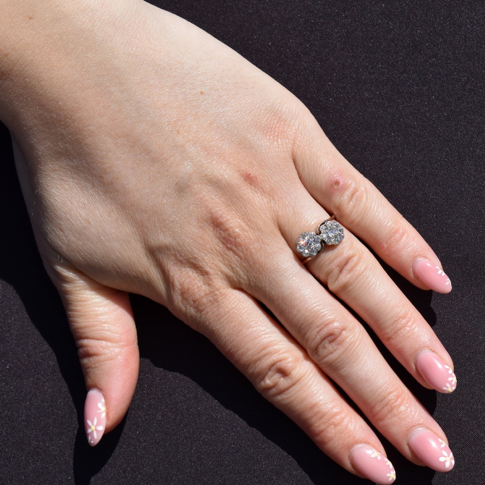 An antique diamond ring featuring two circular daisy clusters on a crossover metal twist band. View X