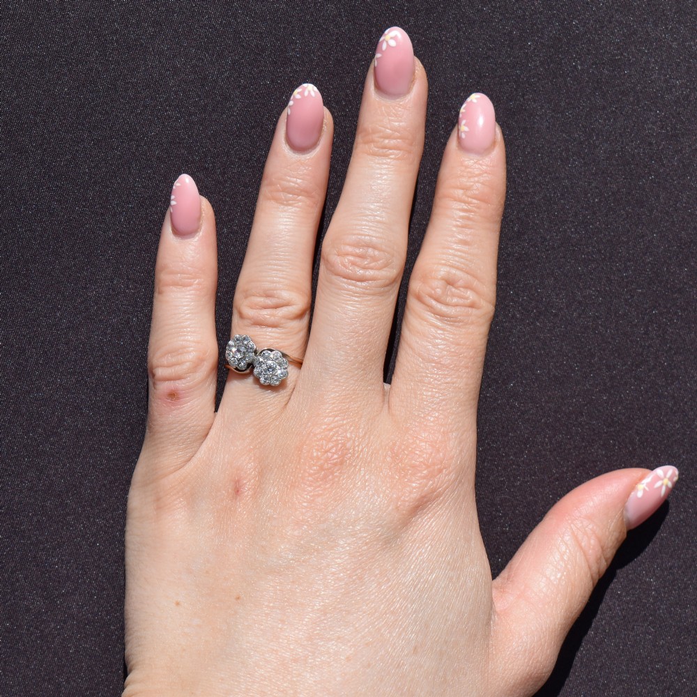 An antique diamond ring featuring two circular daisy clusters on a crossover metal twist band. View XI