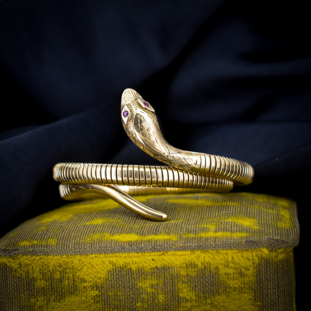 A vintage coiled 9ct yellow gold snake bangle featuring hand-engraved head detailing and red gemstone eyes.