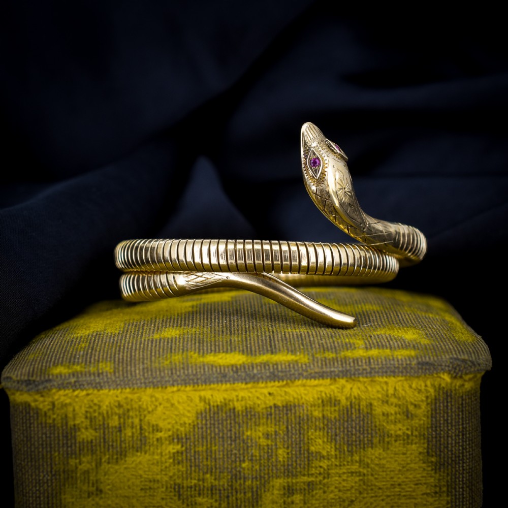 A vintage coiled 9ct yellow gold snake bangle featuring hand-engraved head detailing and red gemstone eyes. View II