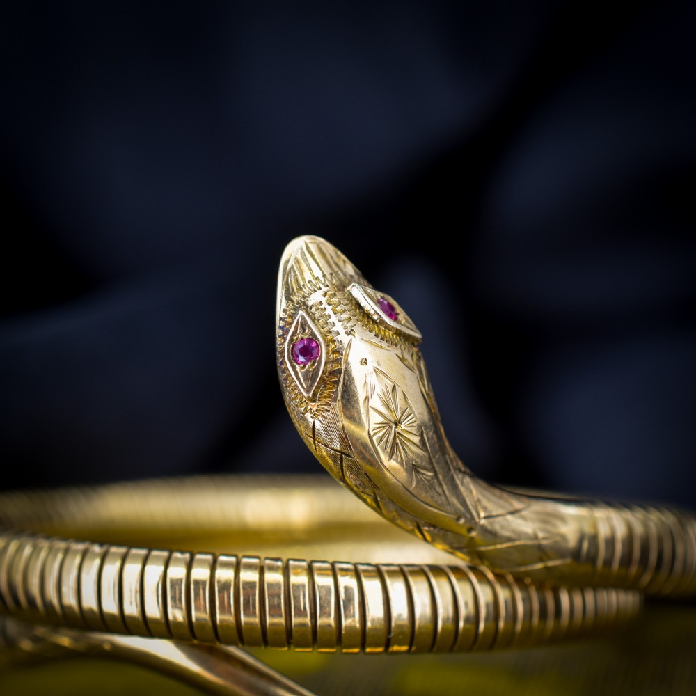 A vintage coiled 9ct yellow gold snake bangle featuring hand-engraved head detailing and red gemstone eyes. View III