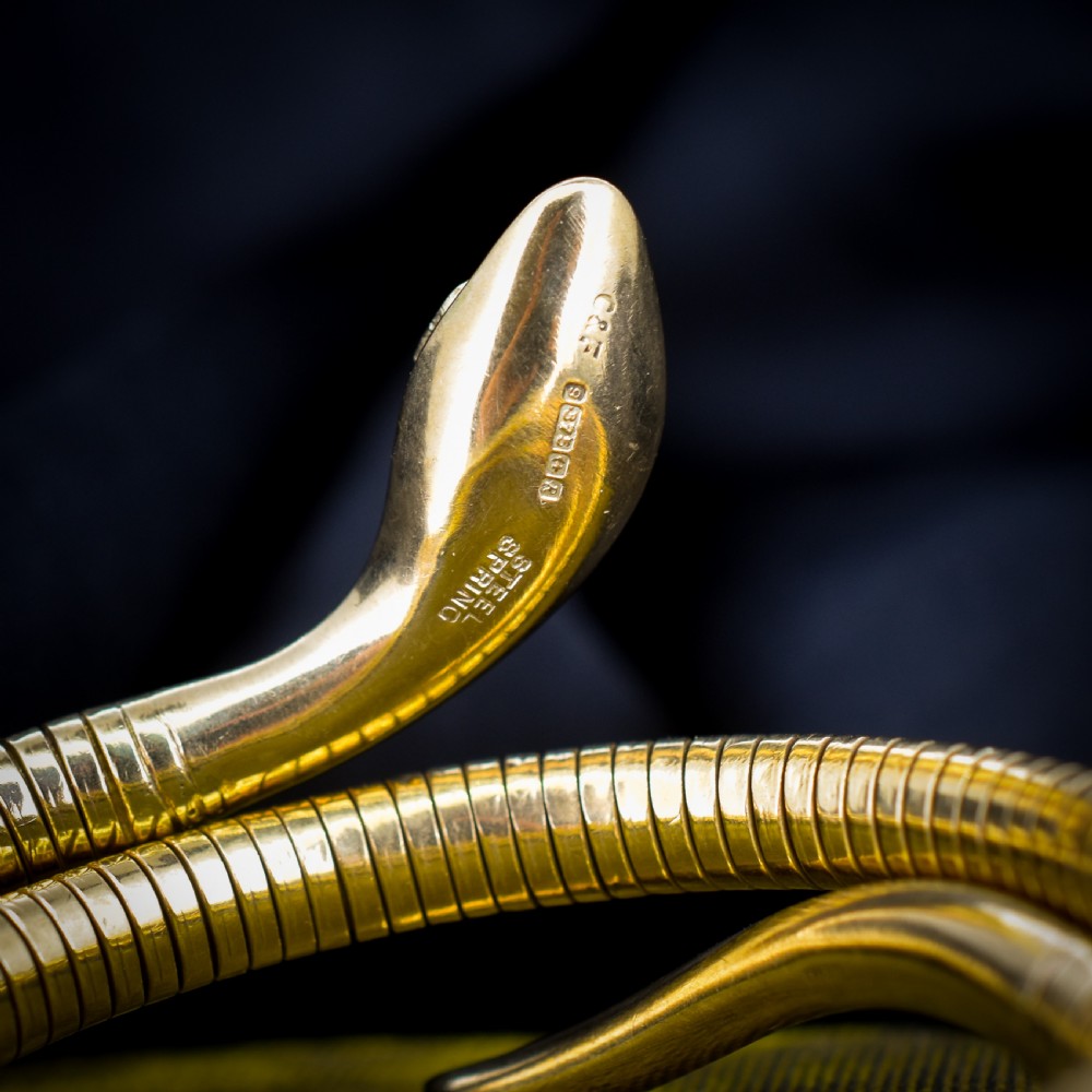 A vintage coiled 9ct yellow gold snake bangle featuring hand-engraved head detailing and red gemstone eyes. View IV