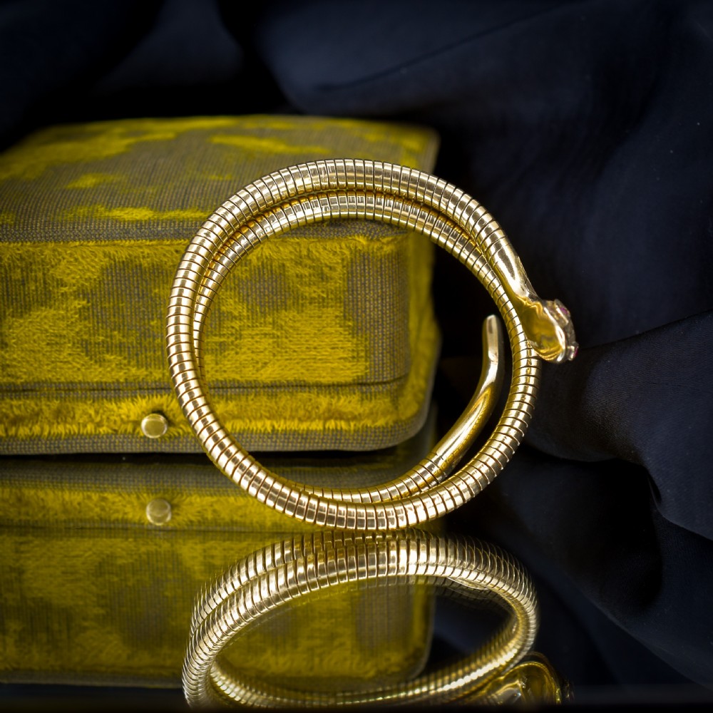 A vintage coiled 9ct yellow gold snake bangle featuring hand-engraved head detailing and red gemstone eyes. View V