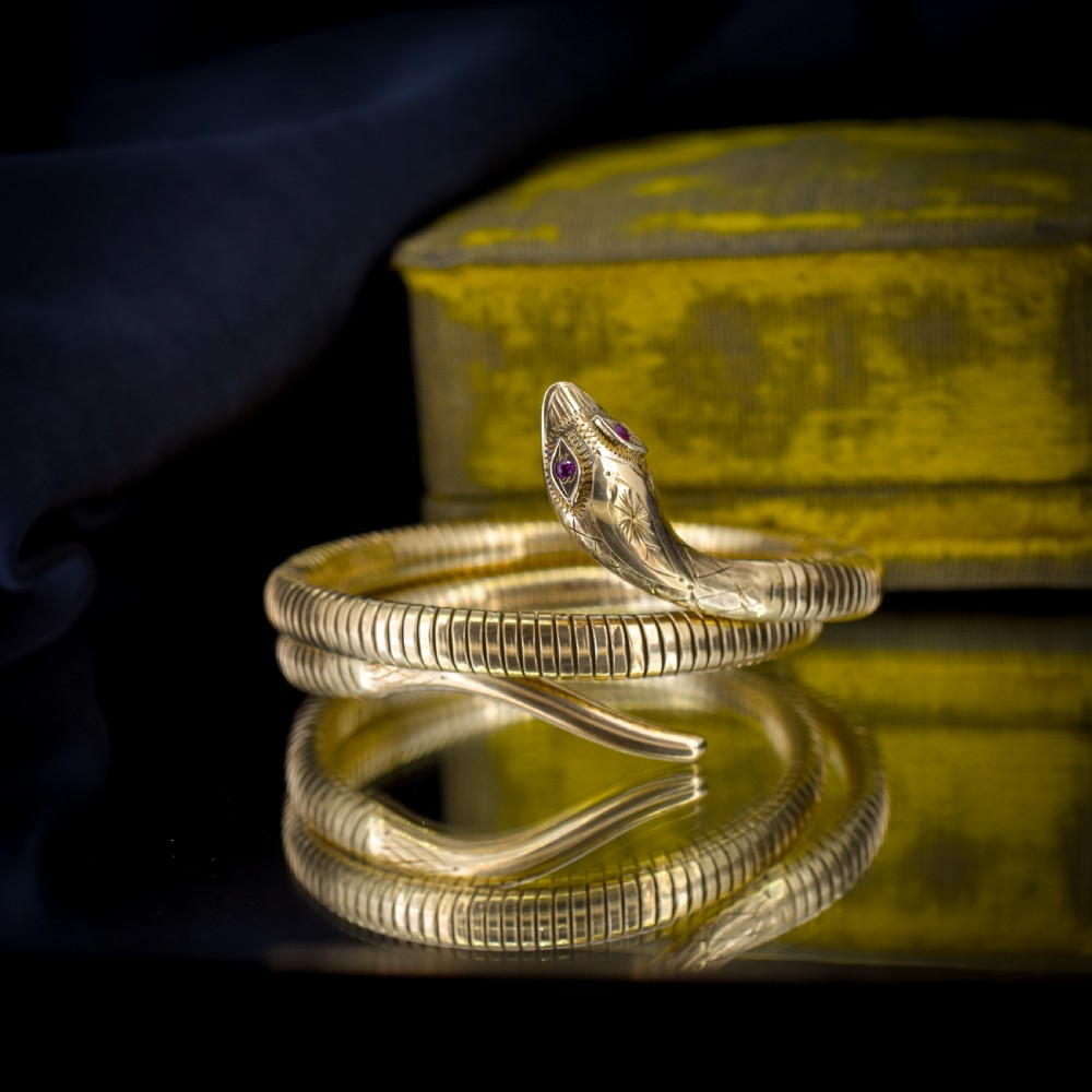 A vintage coiled 9ct yellow gold snake bangle featuring hand-engraved head detailing and red gemstone eyes. View VI