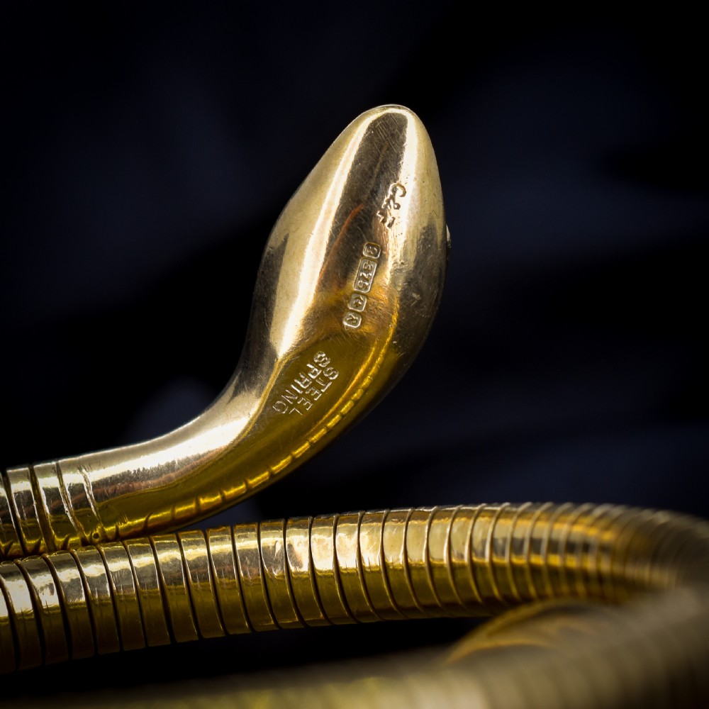 A vintage coiled 9ct yellow gold snake bangle featuring hand-engraved head detailing and red gemstone eyes. View VII