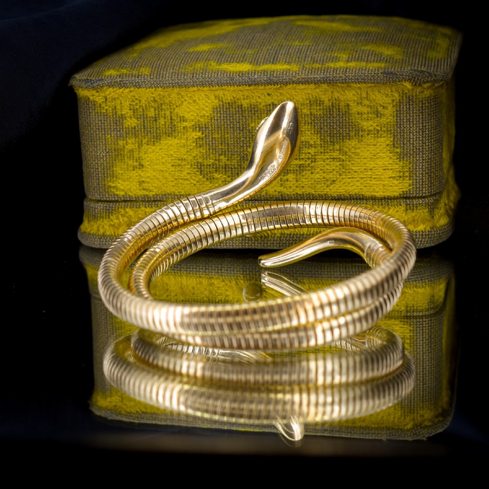A vintage coiled 9ct yellow gold snake bangle featuring hand-engraved head detailing and red gemstone eyes. View VIII