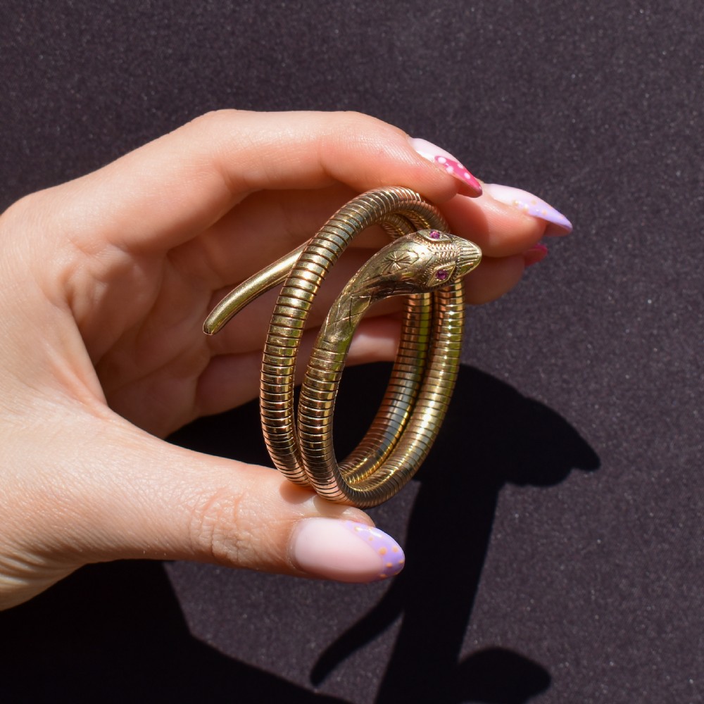 A vintage coiled 9ct yellow gold snake bangle featuring hand-engraved head detailing and red gemstone eyes. View X