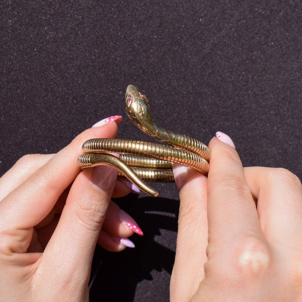 A vintage coiled 9ct yellow gold snake bangle featuring hand-engraved head detailing and red gemstone eyes. View XI