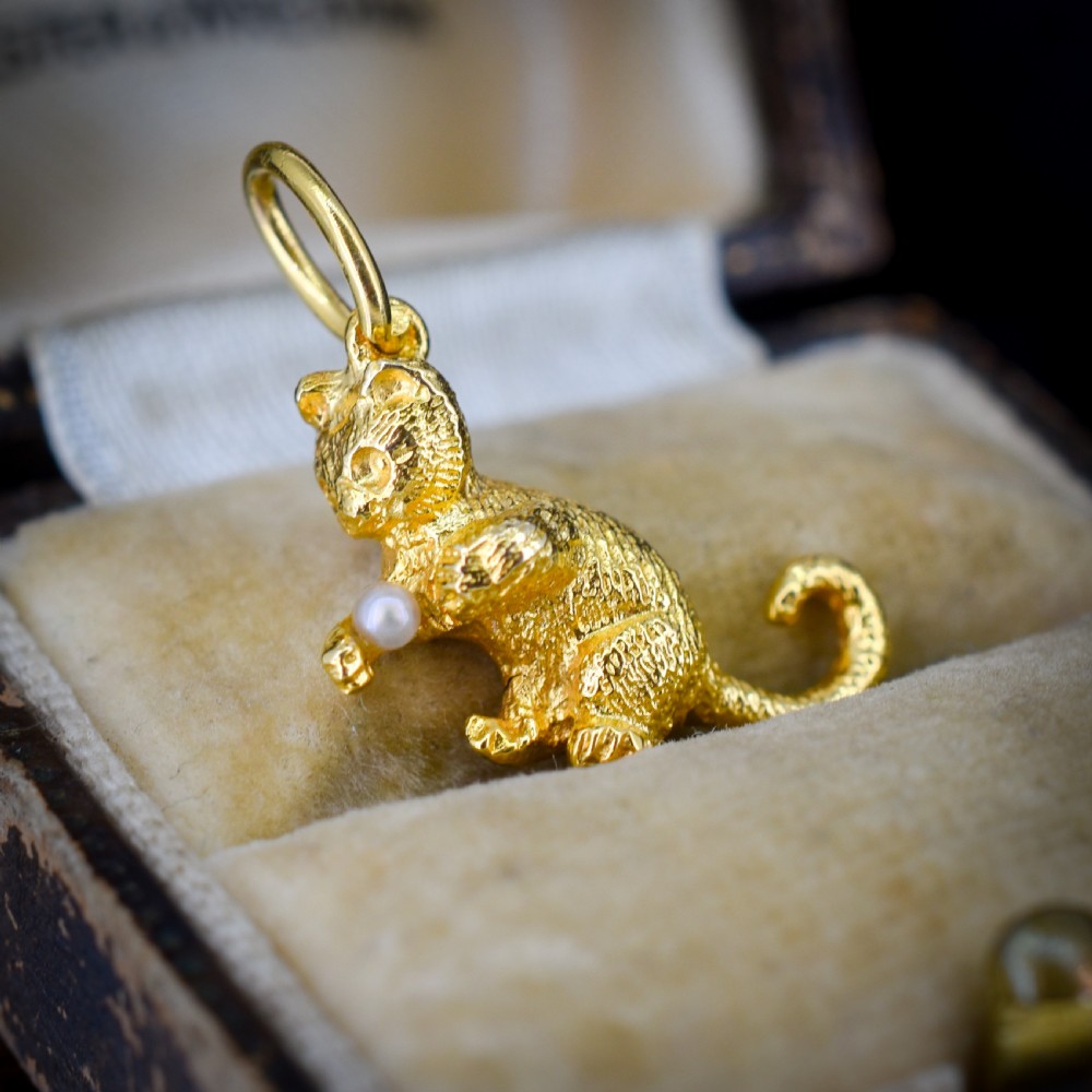 A 9ct yellow gold cat charm in a seated pose with textured fur detail holding a small cultured pearl in its paws.