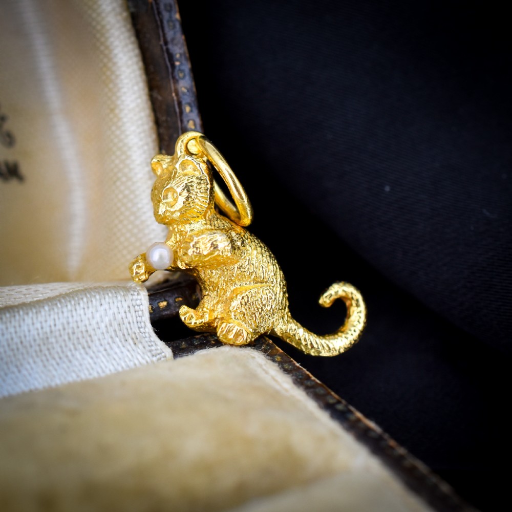 A 9ct yellow gold cat charm in a seated pose with textured fur detail holding a small cultured pearl in its paws. View V