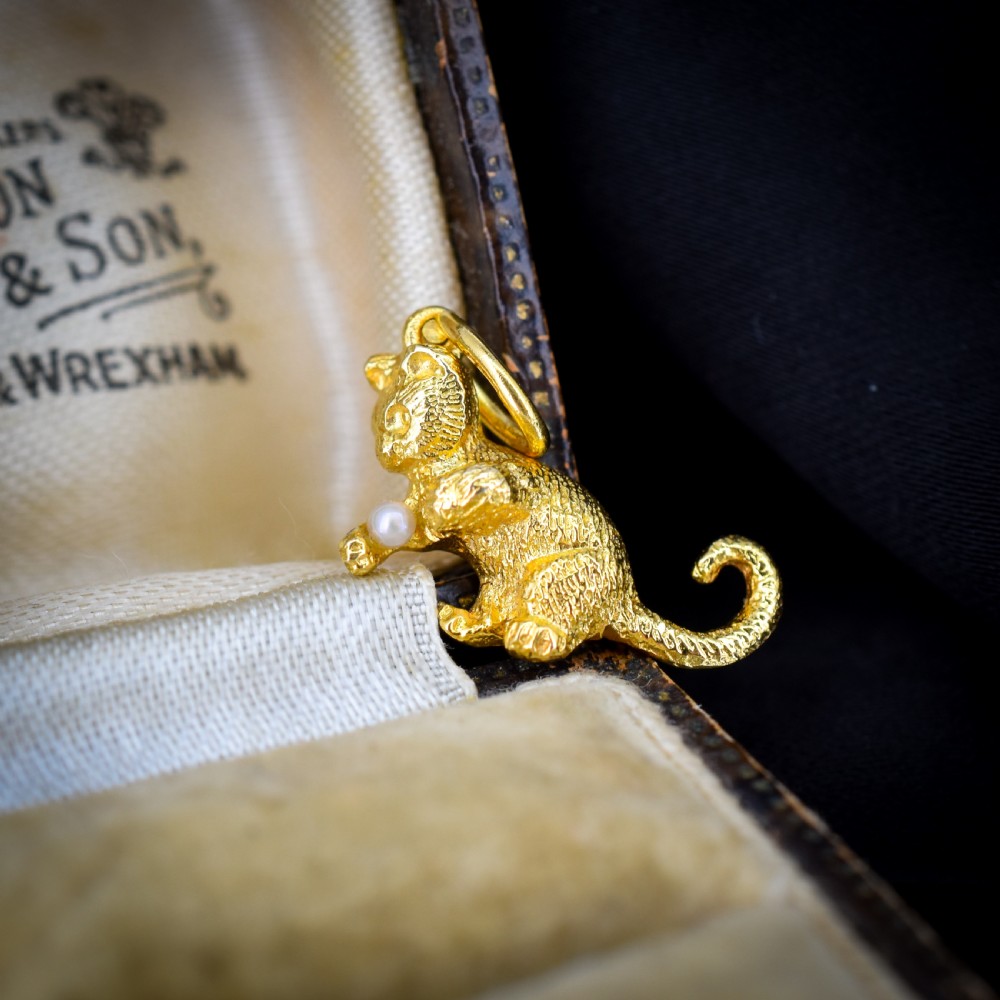 A 9ct yellow gold cat charm in a seated pose with textured fur detail holding a small cultured pearl in its paws. View VI