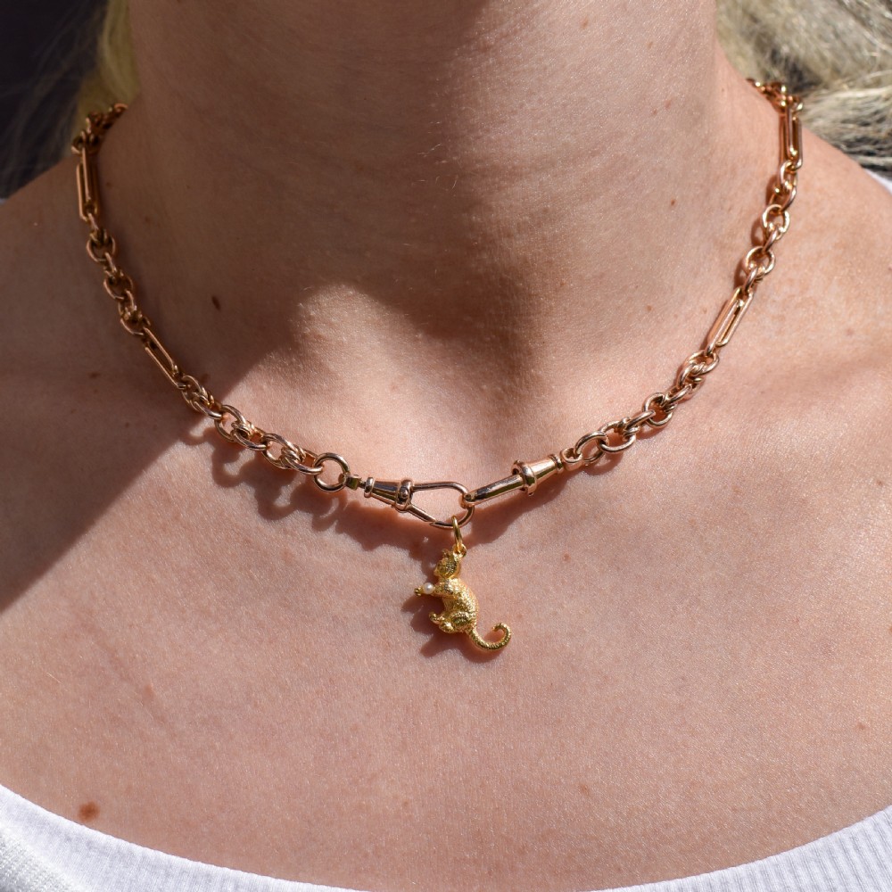 A 9ct yellow gold cat charm in a seated pose with textured fur detail holding a small cultured pearl in its paws. View X