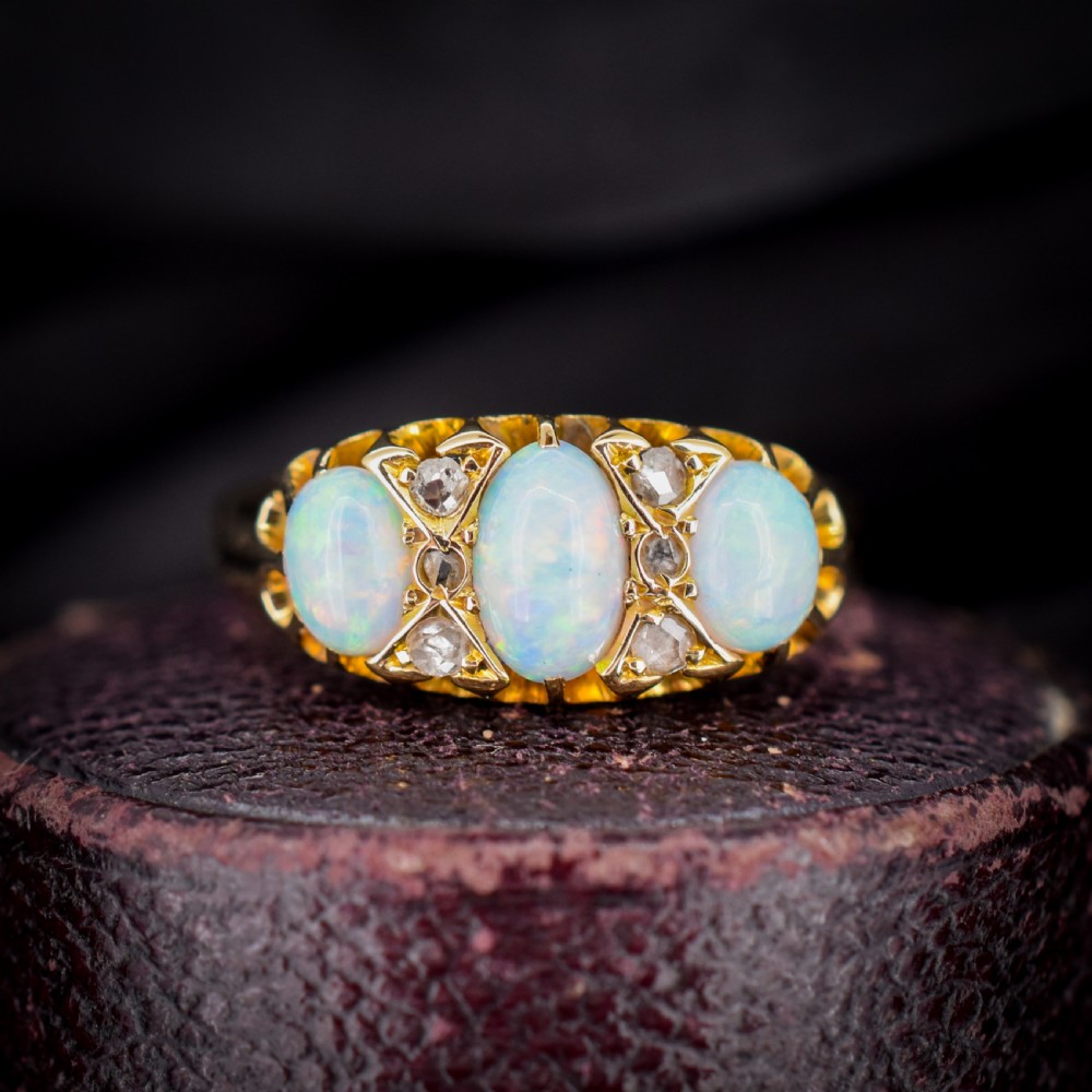 An antique 18ct yellow gold three-stone ring featuring three oval opal cabochons flanked by small diamond accents within a carved mount.