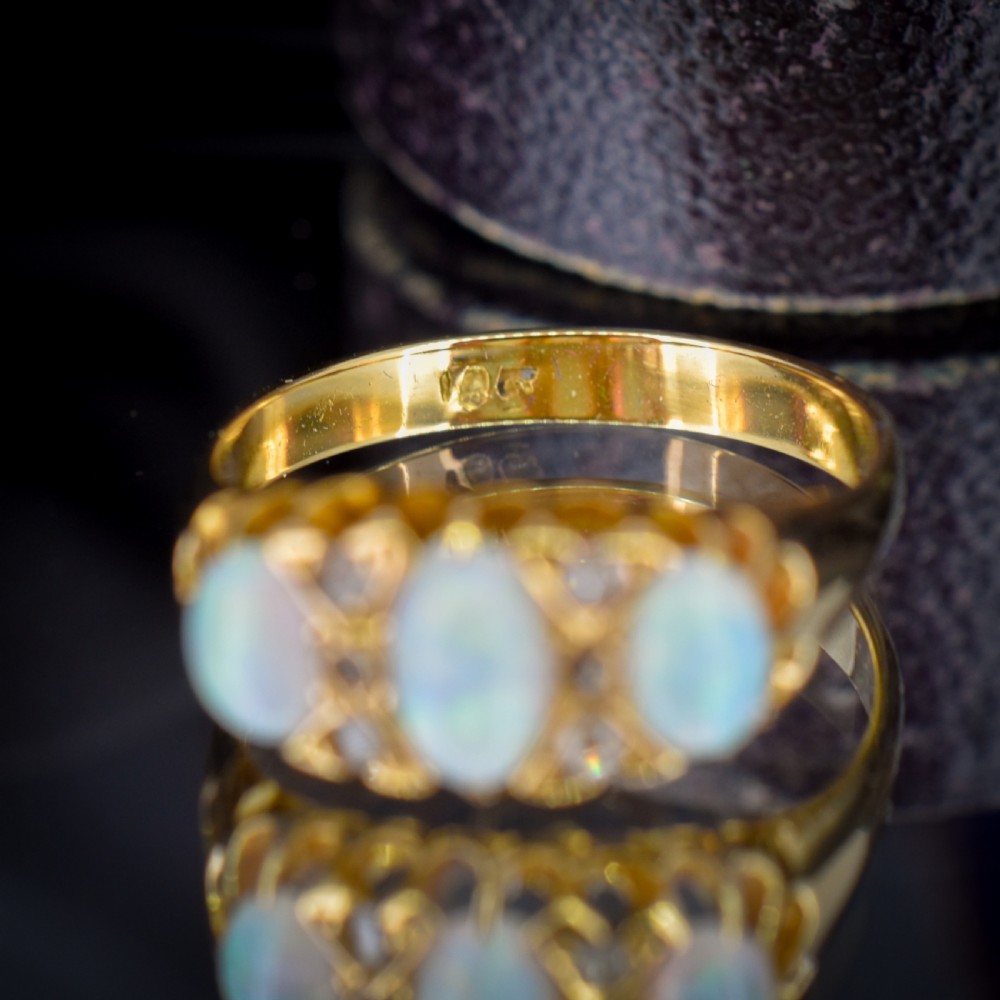 An antique 18ct yellow gold three-stone ring featuring three oval opal cabochons flanked by small diamond accents within a carved mount. View II