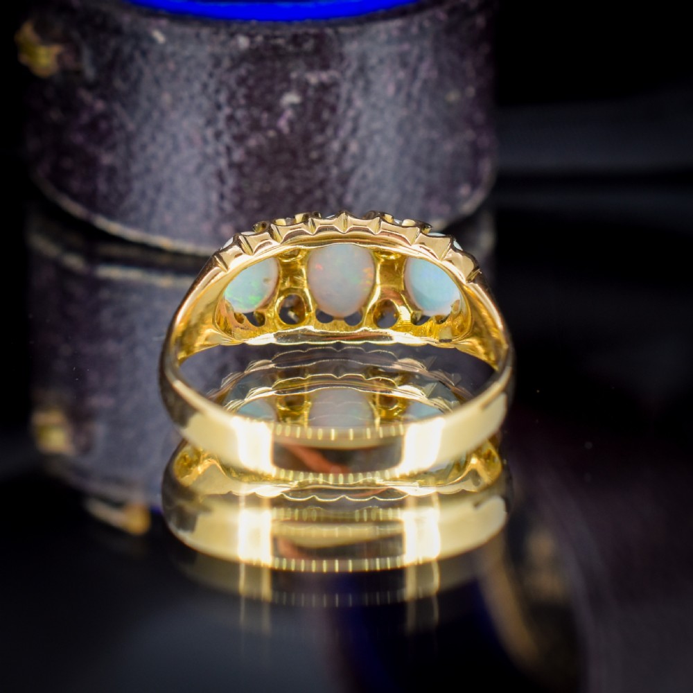 An antique 18ct yellow gold three-stone ring featuring three oval opal cabochons flanked by small diamond accents within a carved mount. View III