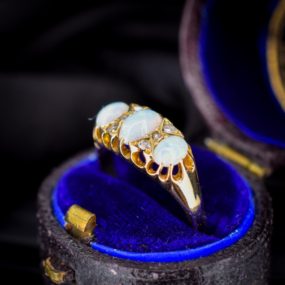 An antique 18ct yellow gold three-stone ring featuring three oval opal cabochons flanked by small diamond accents within a carved mount. View VI