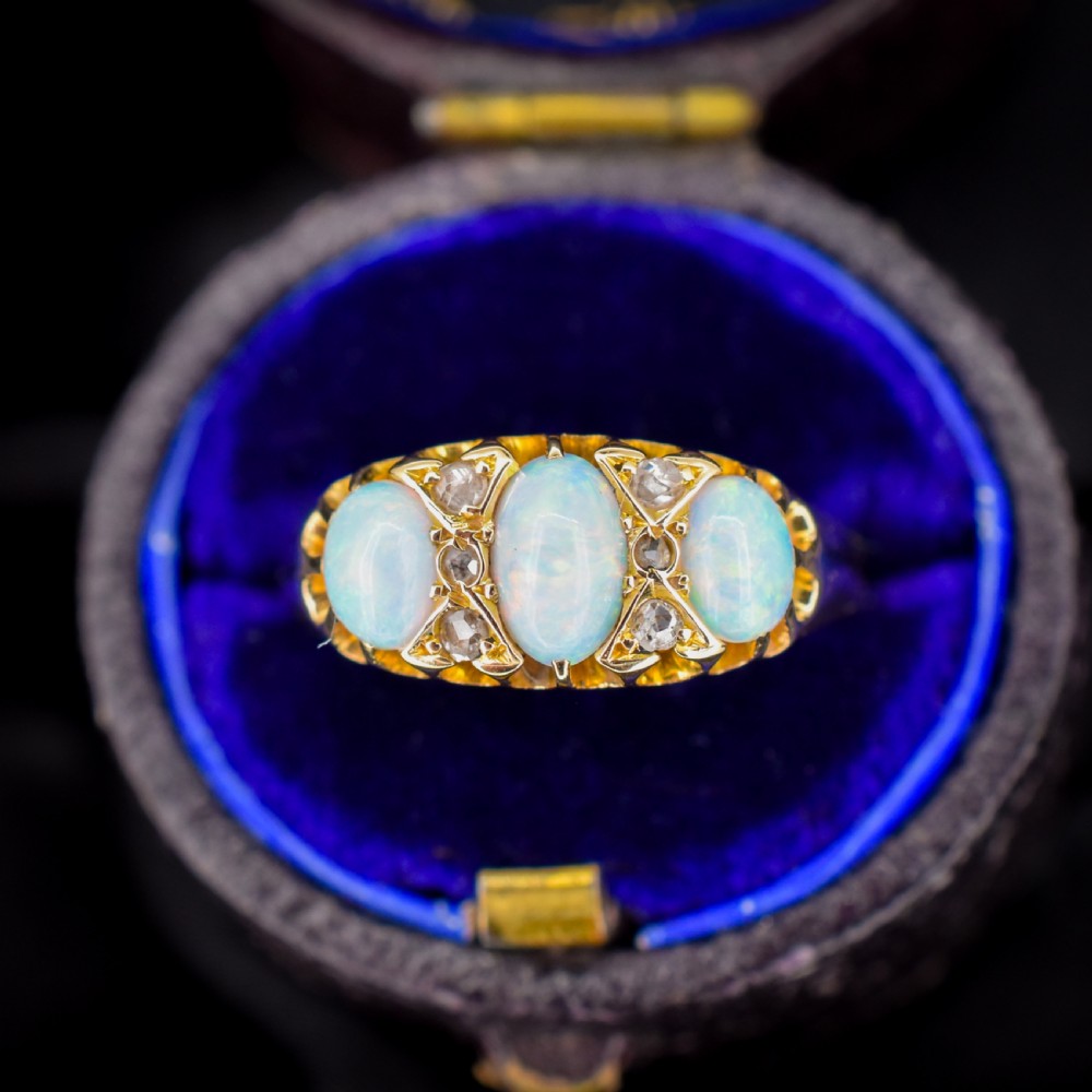 An antique 18ct yellow gold three-stone ring featuring three oval opal cabochons flanked by small diamond accents within a carved mount. View VII