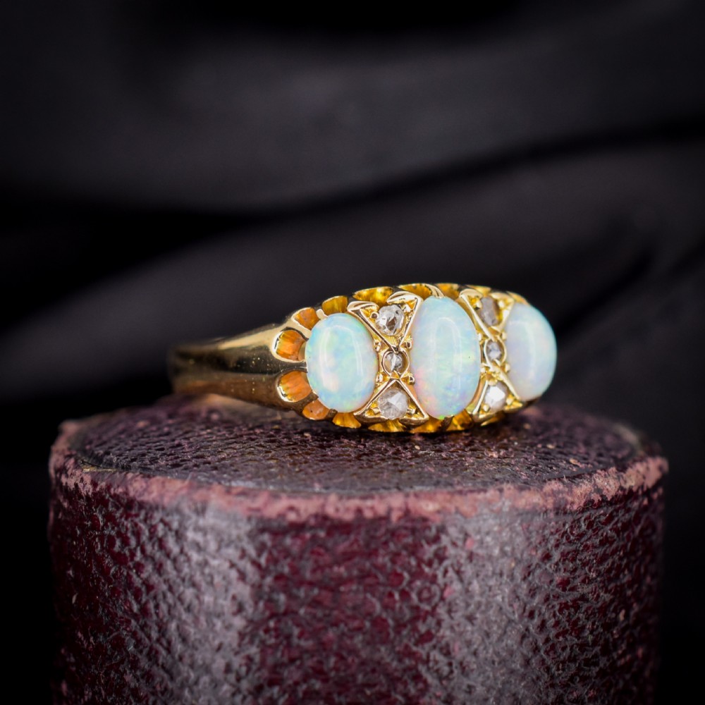 An antique 18ct yellow gold three-stone ring featuring three oval opal cabochons flanked by small diamond accents within a carved mount. View VIII