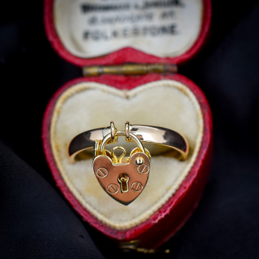 A 9ct yellow gold band ring featuring a dangling heart-shaped padlock charm suspended from two central loops. View II