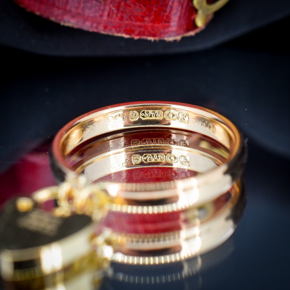 A 9ct yellow gold band ring featuring a dangling heart-shaped padlock charm suspended from two central loops. View VII
