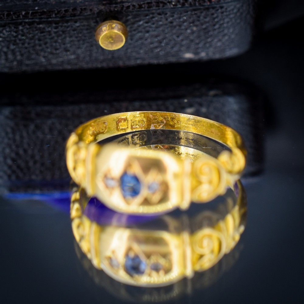 An 18ct yellow gold gypsy ring featuring a central oval sapphire and two round diamonds set in starburst engravings with scrolled shoulder details. View VII