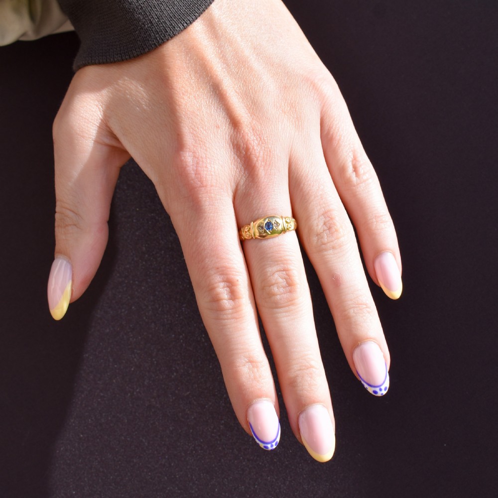 An 18ct yellow gold gypsy ring featuring a central oval sapphire and two round diamonds set in starburst engravings with scrolled shoulder details. View XI