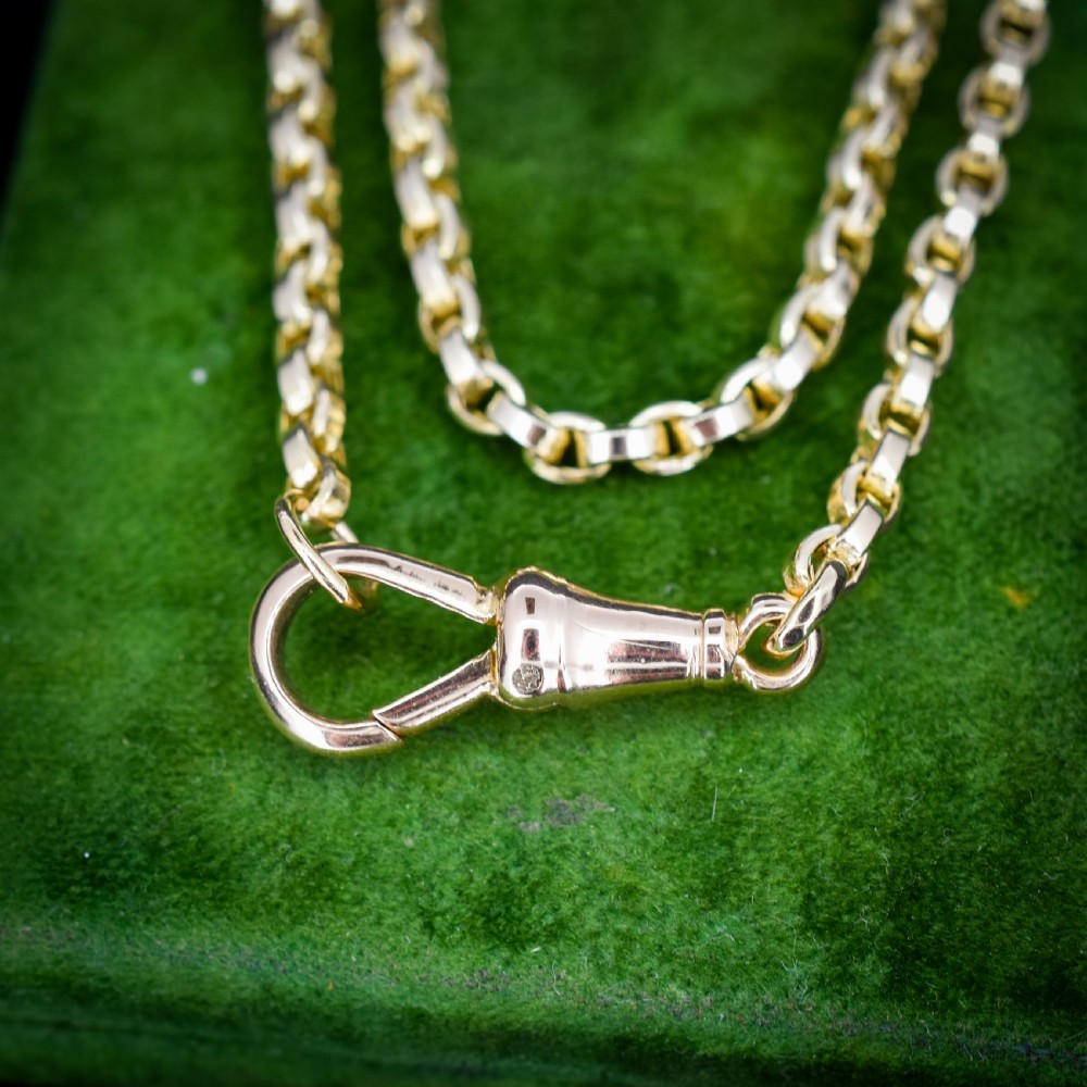 An antique 9ct yellow gold chain necklace featuring uniform oval links and a dog clip clasp displayed on a green velvet surface. View II