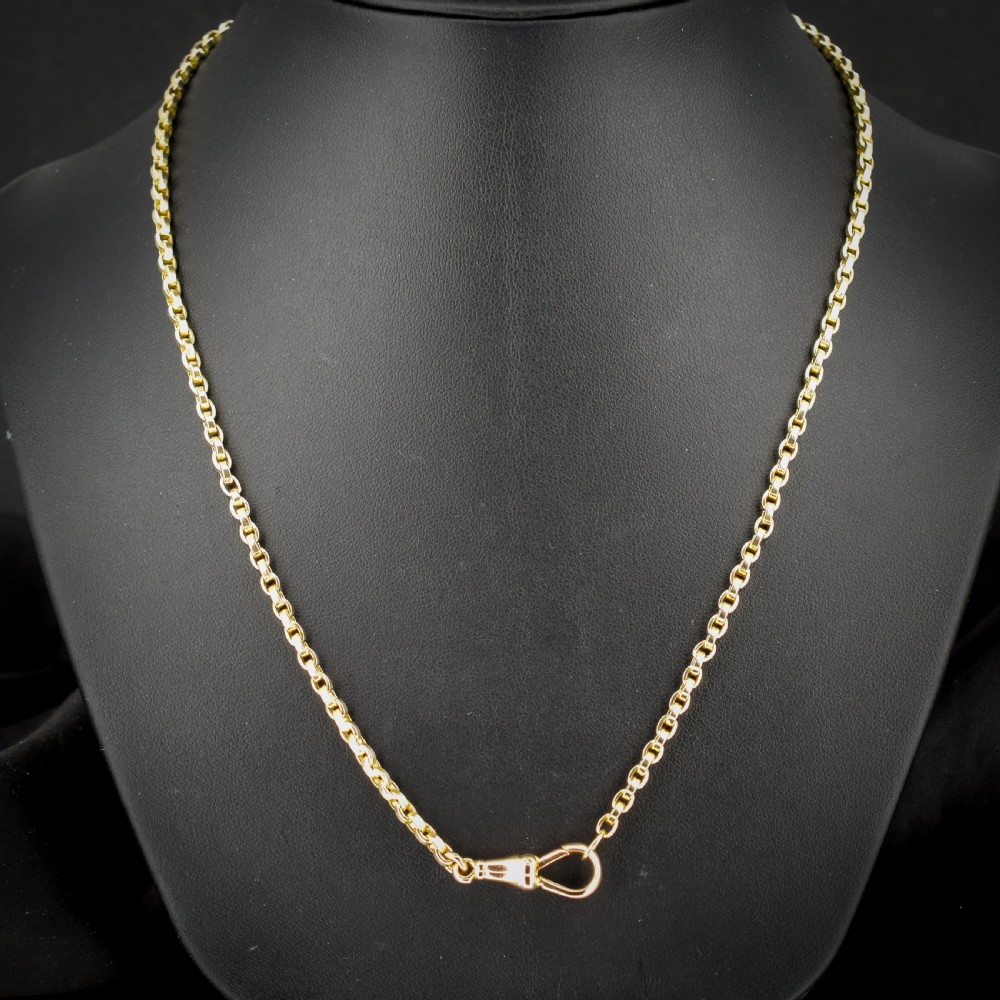 An antique 9ct yellow gold chain necklace featuring uniform oval links and a dog clip clasp displayed on a green velvet surface. View V