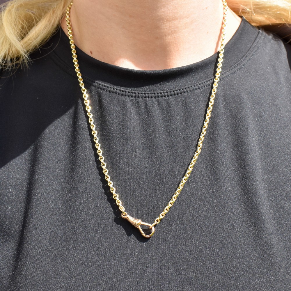 An antique 9ct yellow gold chain necklace featuring uniform oval links and a dog clip clasp displayed on a green velvet surface. View VIII