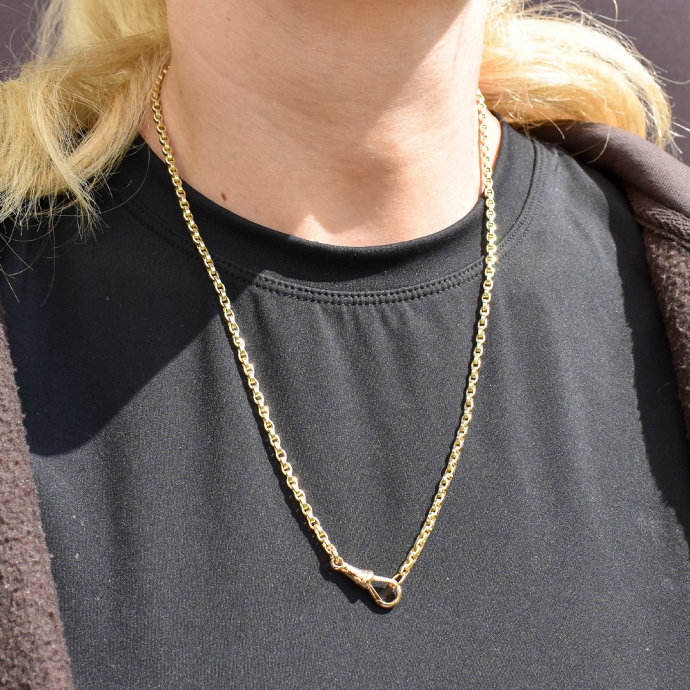 An antique 9ct yellow gold chain necklace featuring uniform oval links and a dog clip clasp displayed on a green velvet surface. View IX