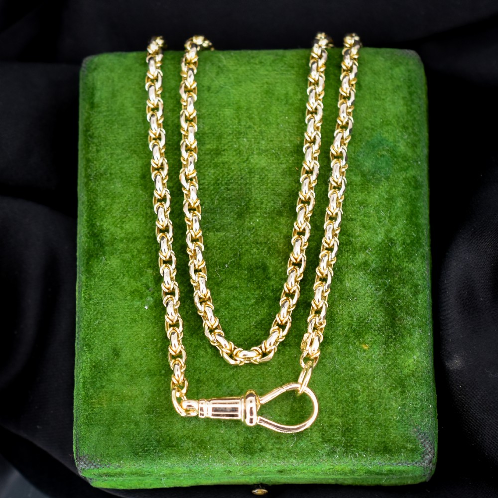 An antique 9ct yellow gold fancy link chain necklace with a dog clip clasp displayed on a green surface.