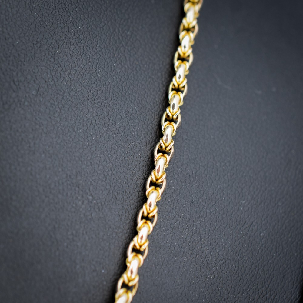 An antique 9ct yellow gold fancy link chain necklace with a dog clip clasp displayed on a green surface. View IV