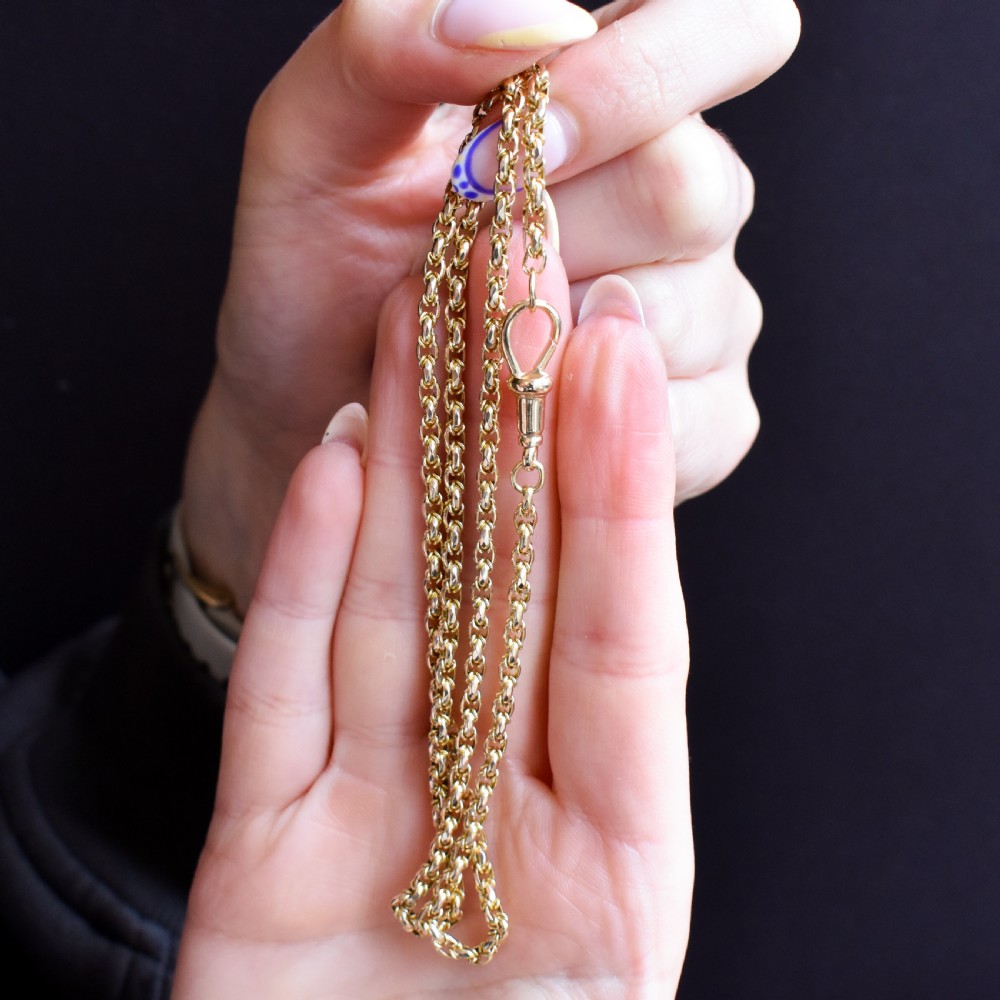 An antique 9ct yellow gold fancy link chain necklace with a dog clip clasp displayed on a green surface. View V