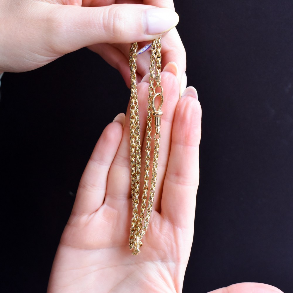 An antique 9ct yellow gold fancy link chain necklace with a dog clip clasp displayed on a green surface. View VI